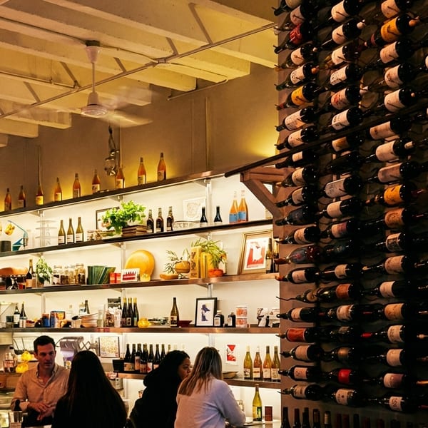 A restaurant interior with a large wine rack, shelves of bottles, and people at a bar.